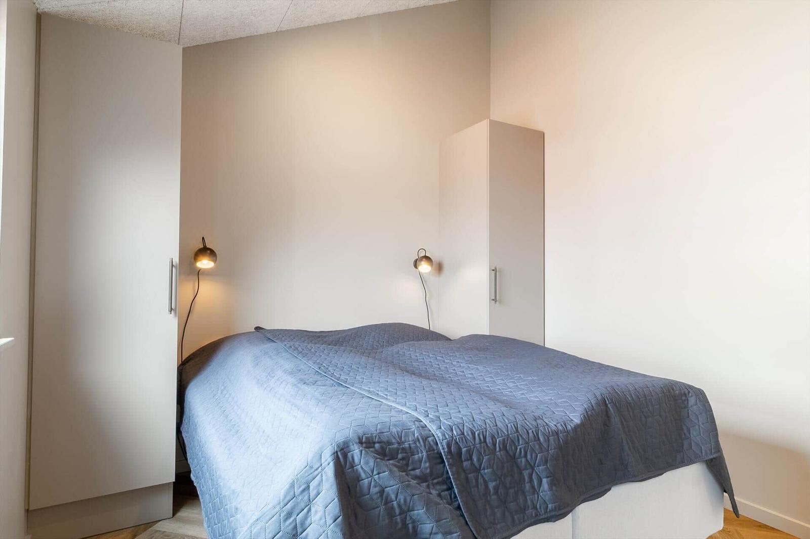 Schlafzimmer mit Bett, blauer Decke und zwei weißen Schränken an den Wänden.