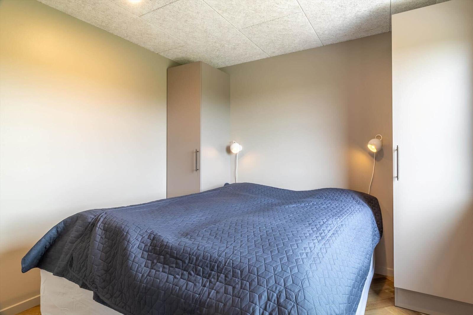 Schlafzimmer mit Bett, blauer Decke und zwei weißen Nachttischen mit Lampen.