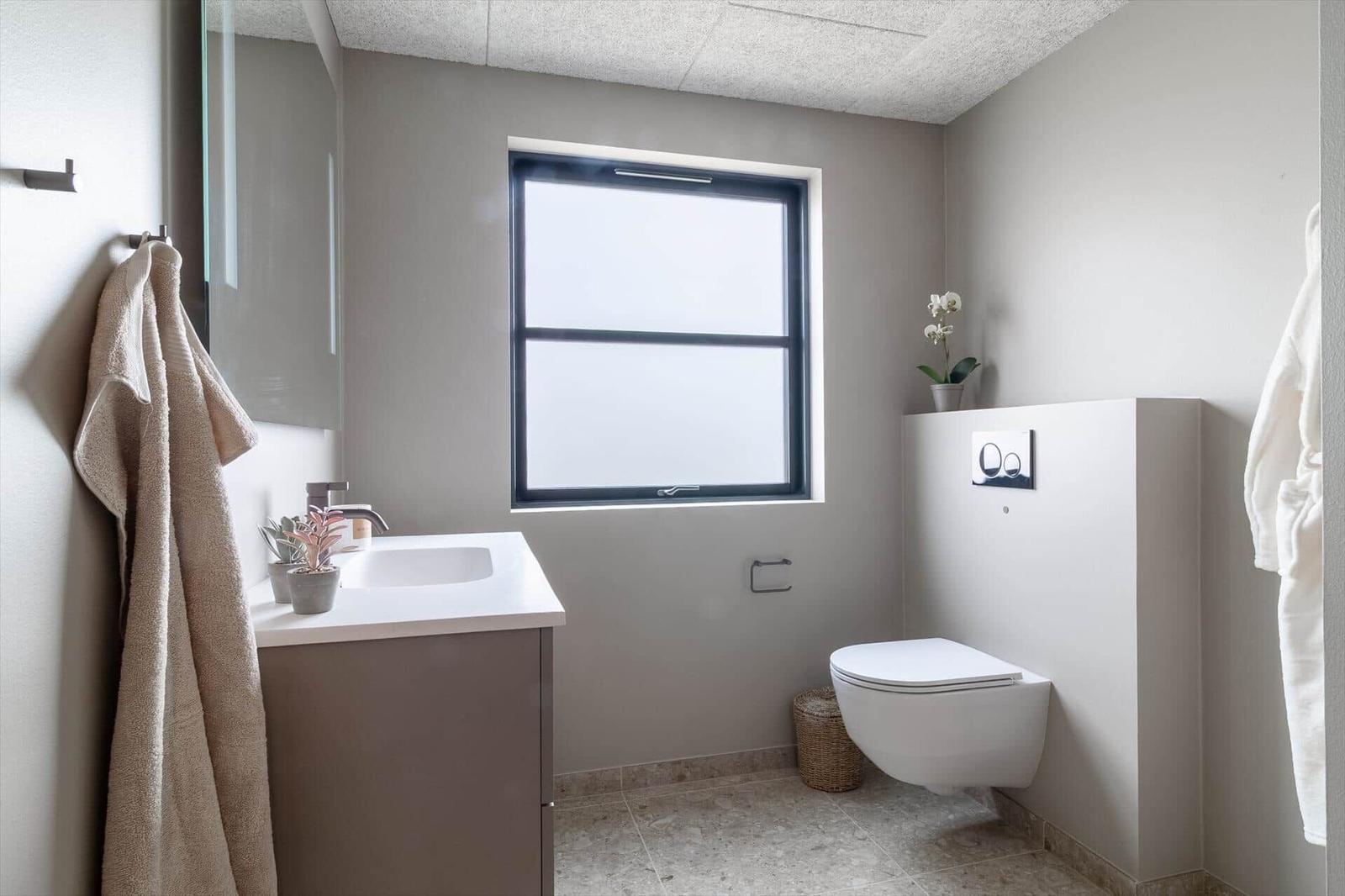 Badezimmer mit Waschbecken, Toilette und Fenster. Handtuch hängt an Wand.