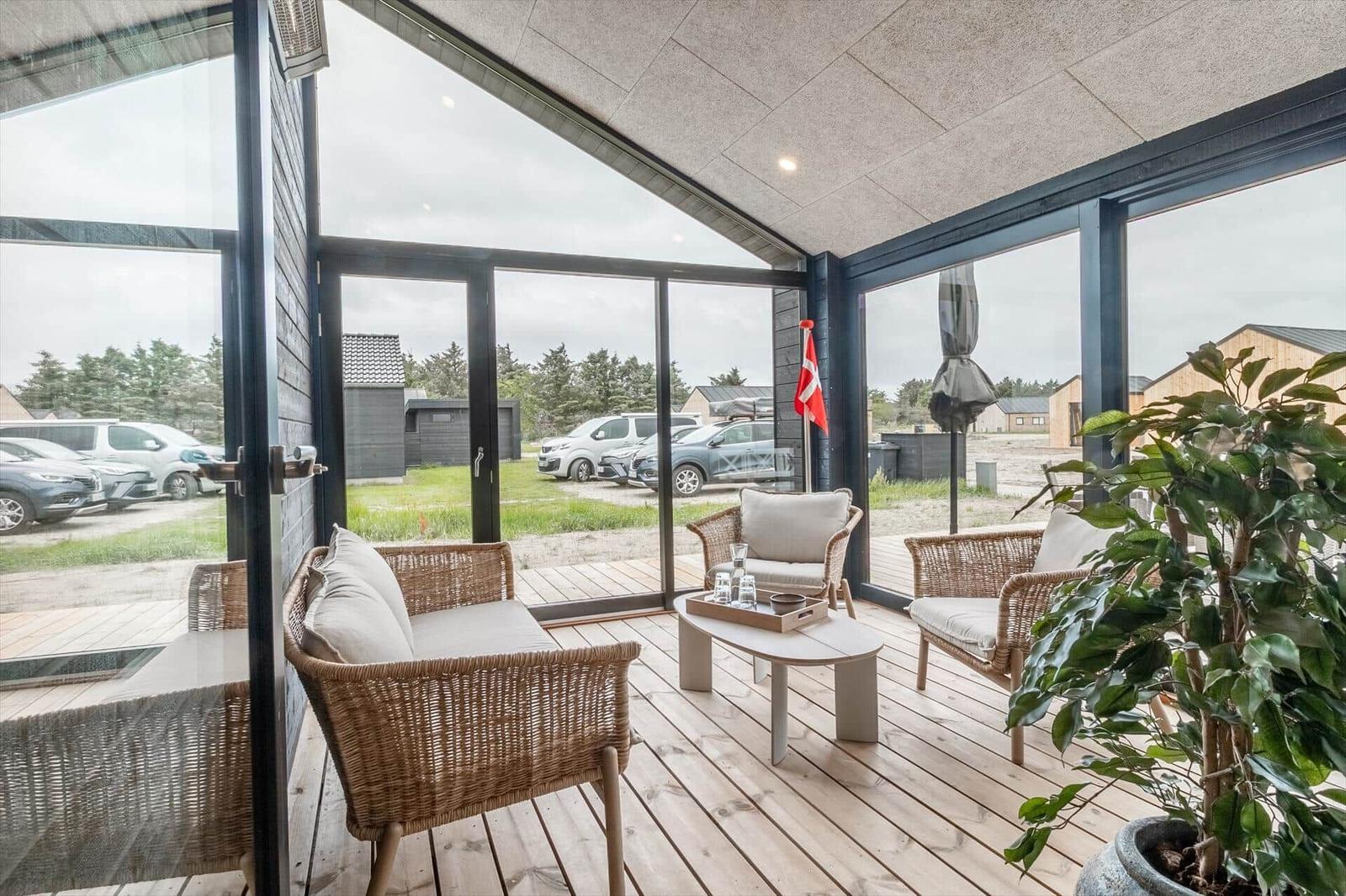 Terrasse mit Rattanmöbeln, Tisch und Pflanze. Durchgehende Glasfront mit Blick auf Parkplatz.