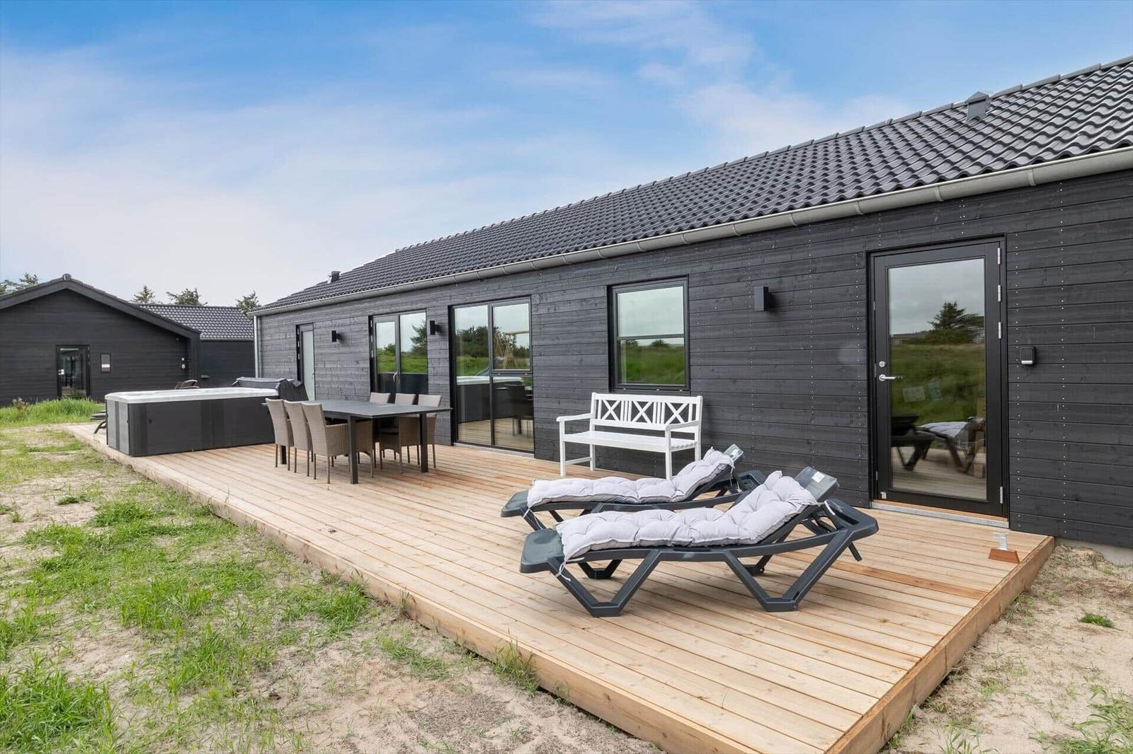 Holzterrasse mit Liegestühlen, Tisch und Whirlpool vor einem modernen Haus.