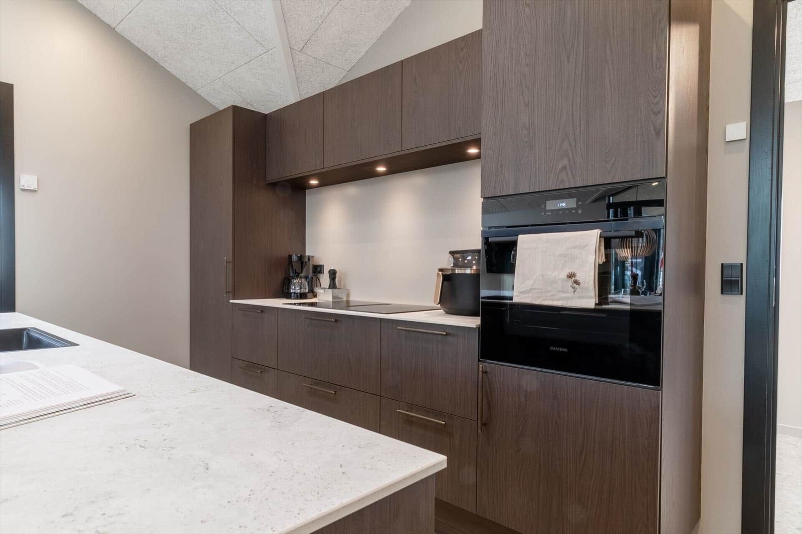 Moderne Küche mit dunklen Schränken, weißer Arbeitsplatte und integriertem Backofen.