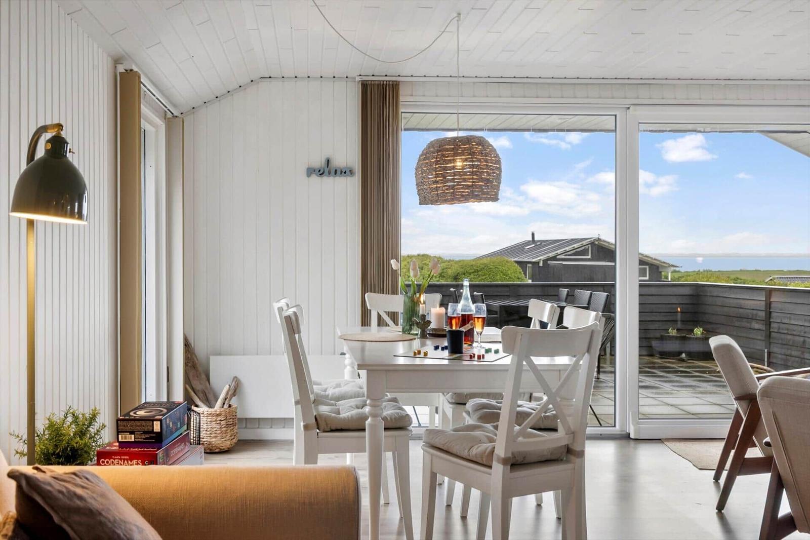 Dining area with view of terrace and sea. White table, chairs, and pendant light.