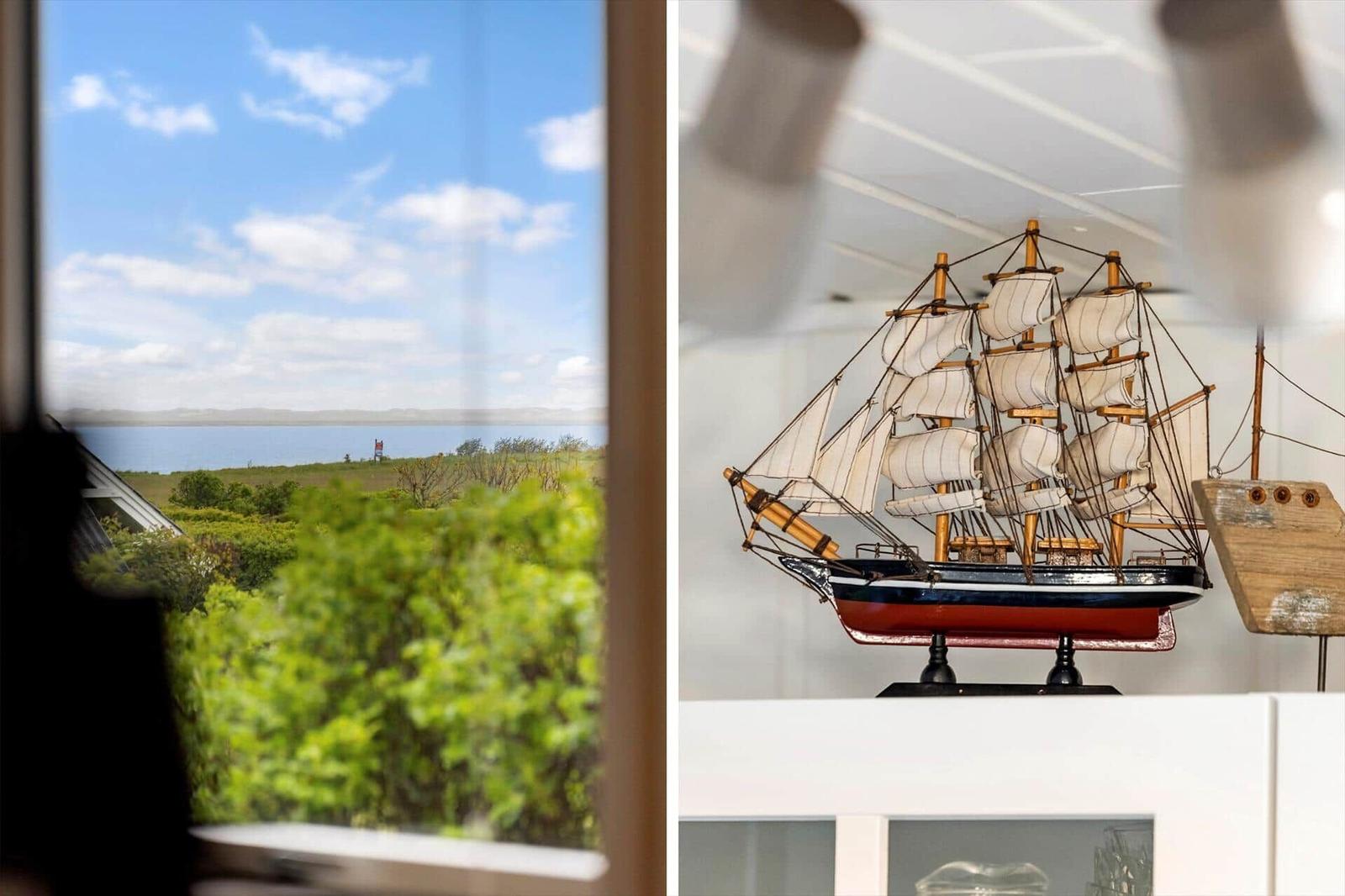 Through the window, a landscape with water and greenery is visible. In the room, a wooden ship model stands.