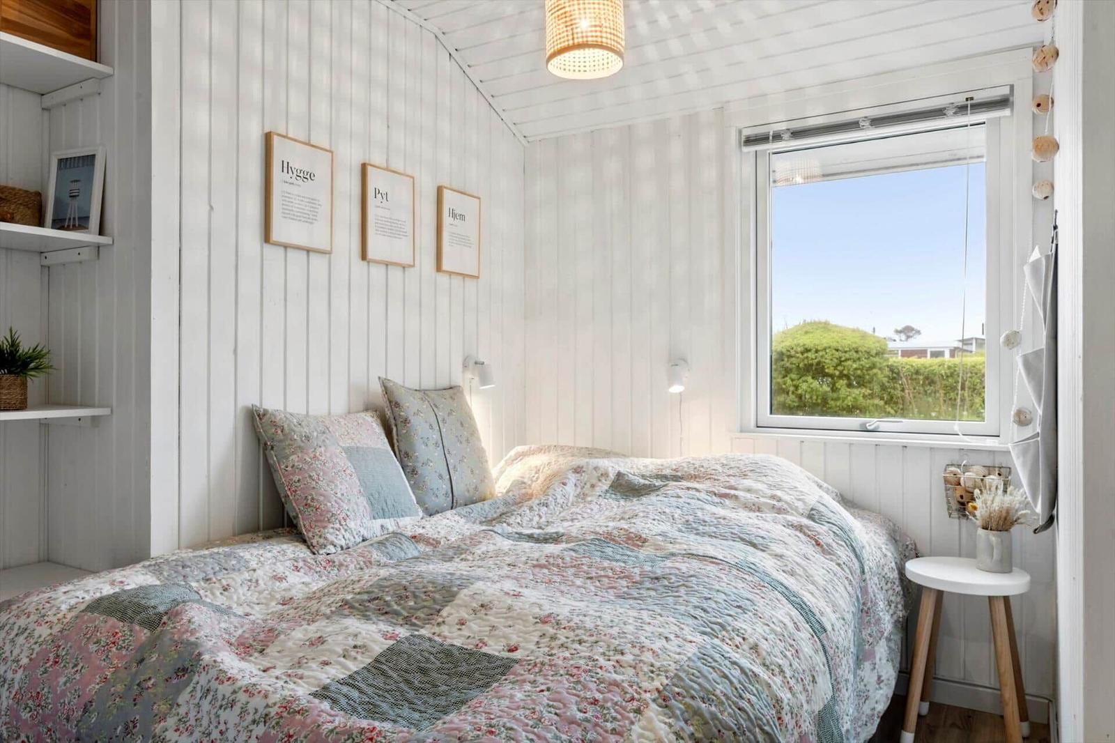 Bedroom with bed, window, and wall shelves. Ceiling and walls are white clad.