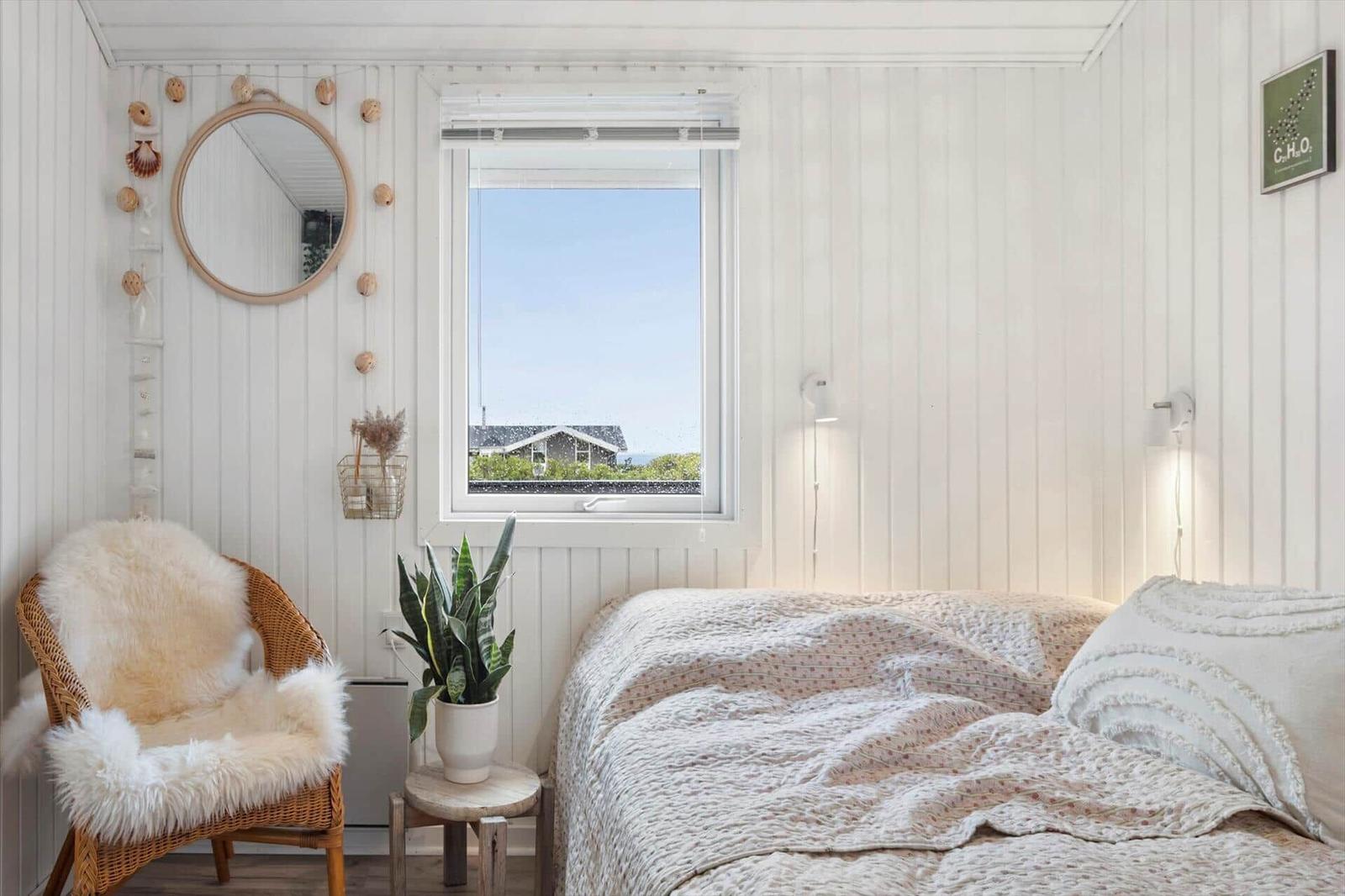 Bedroom with bed, chair, and window view of house and sky.