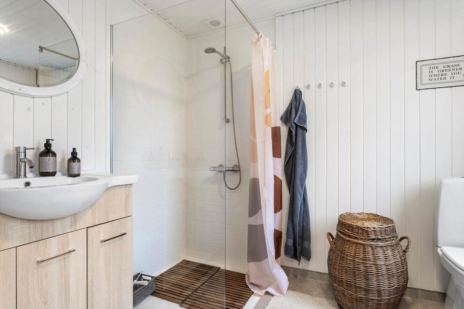 Bathroom with shower, sink and toilet. Wooden vanity, wicker basket and shower curtain.