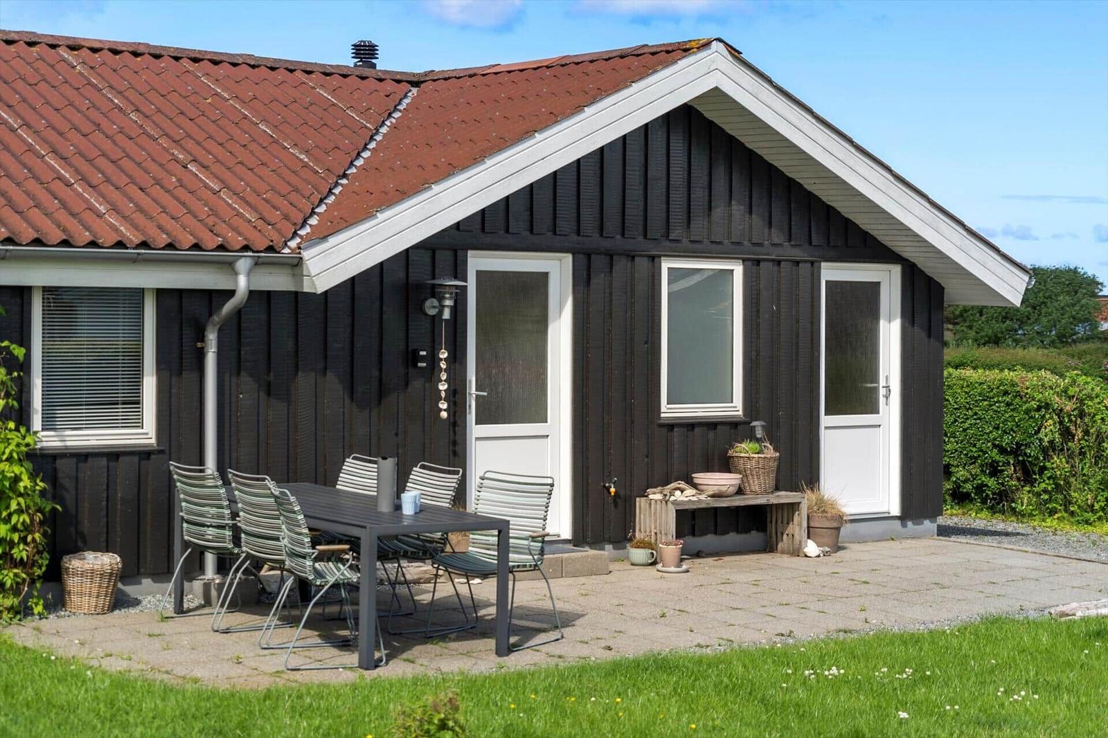 House with terrace, table and chairs, red roof and dark facade.