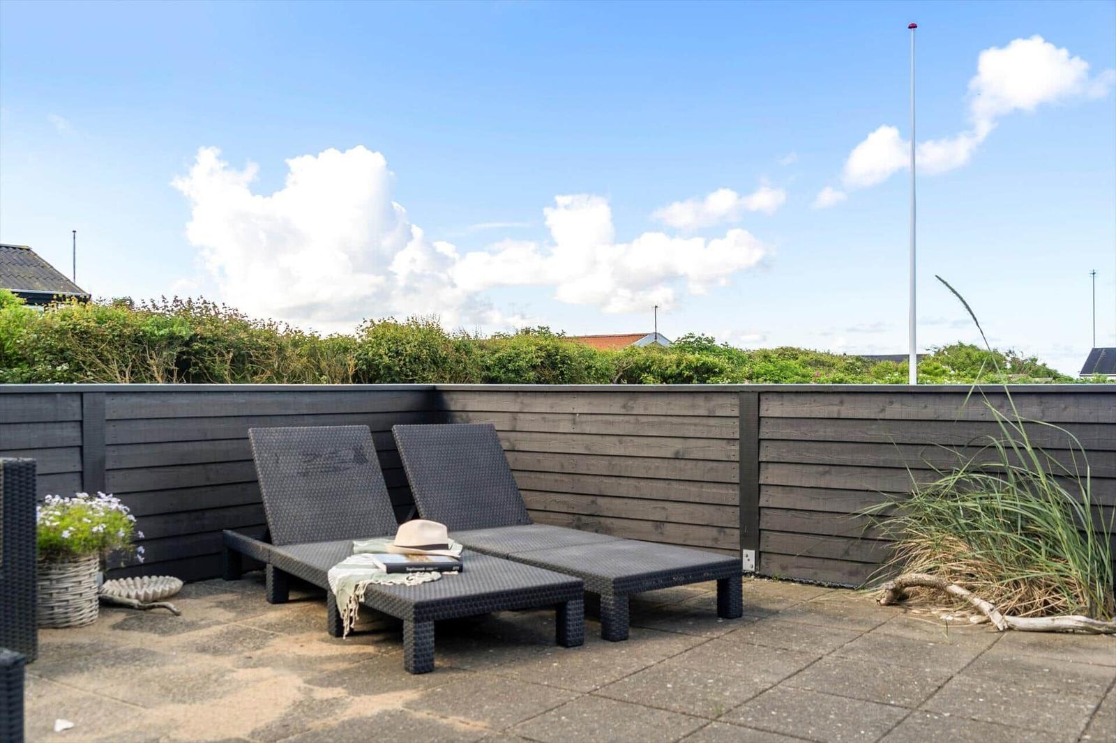 Terrace with two lounge chairs, wooden border, and view of greenery.