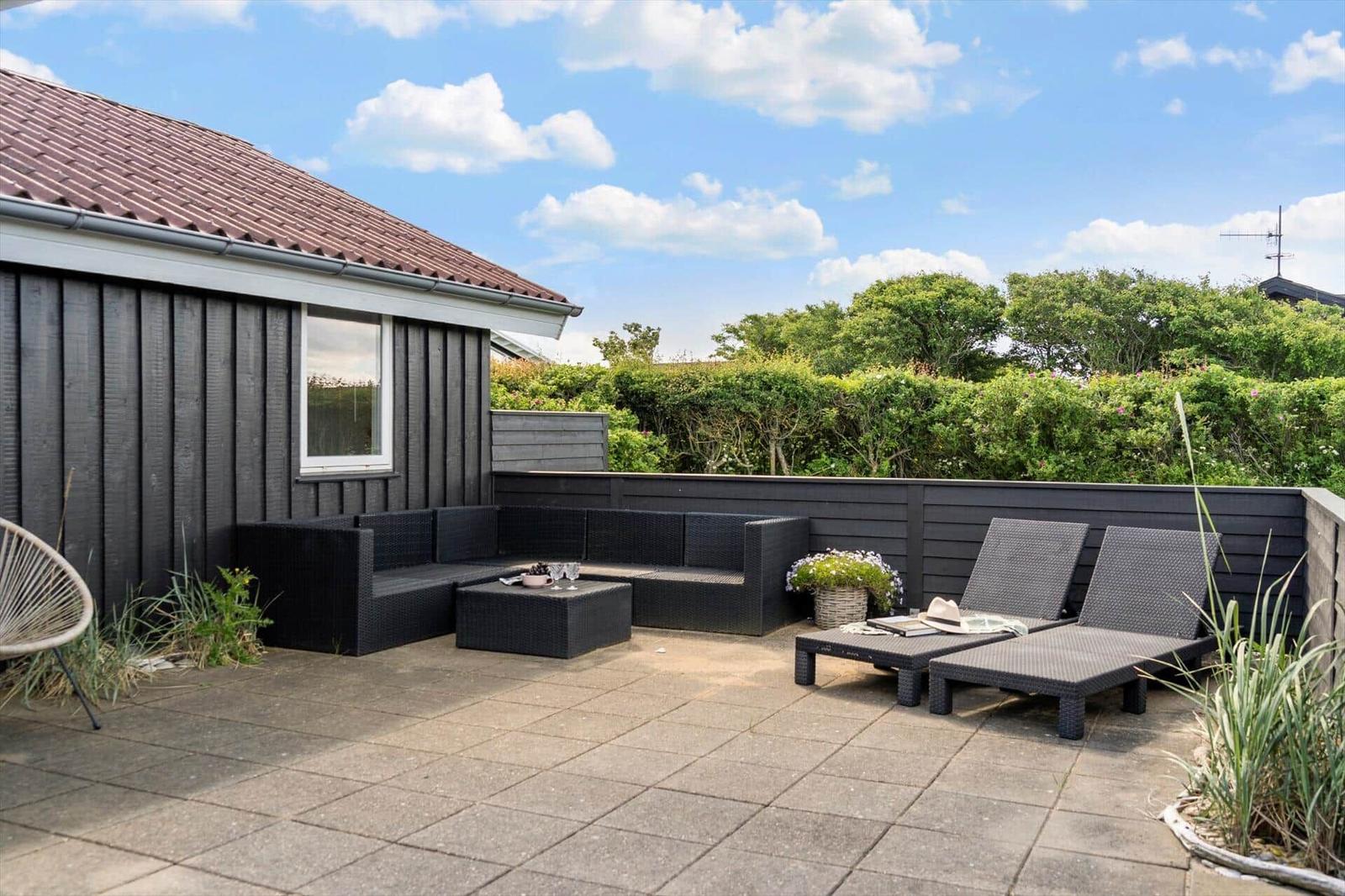Terrace with seating group and sun loungers. Backyard with hedge and blue sky.