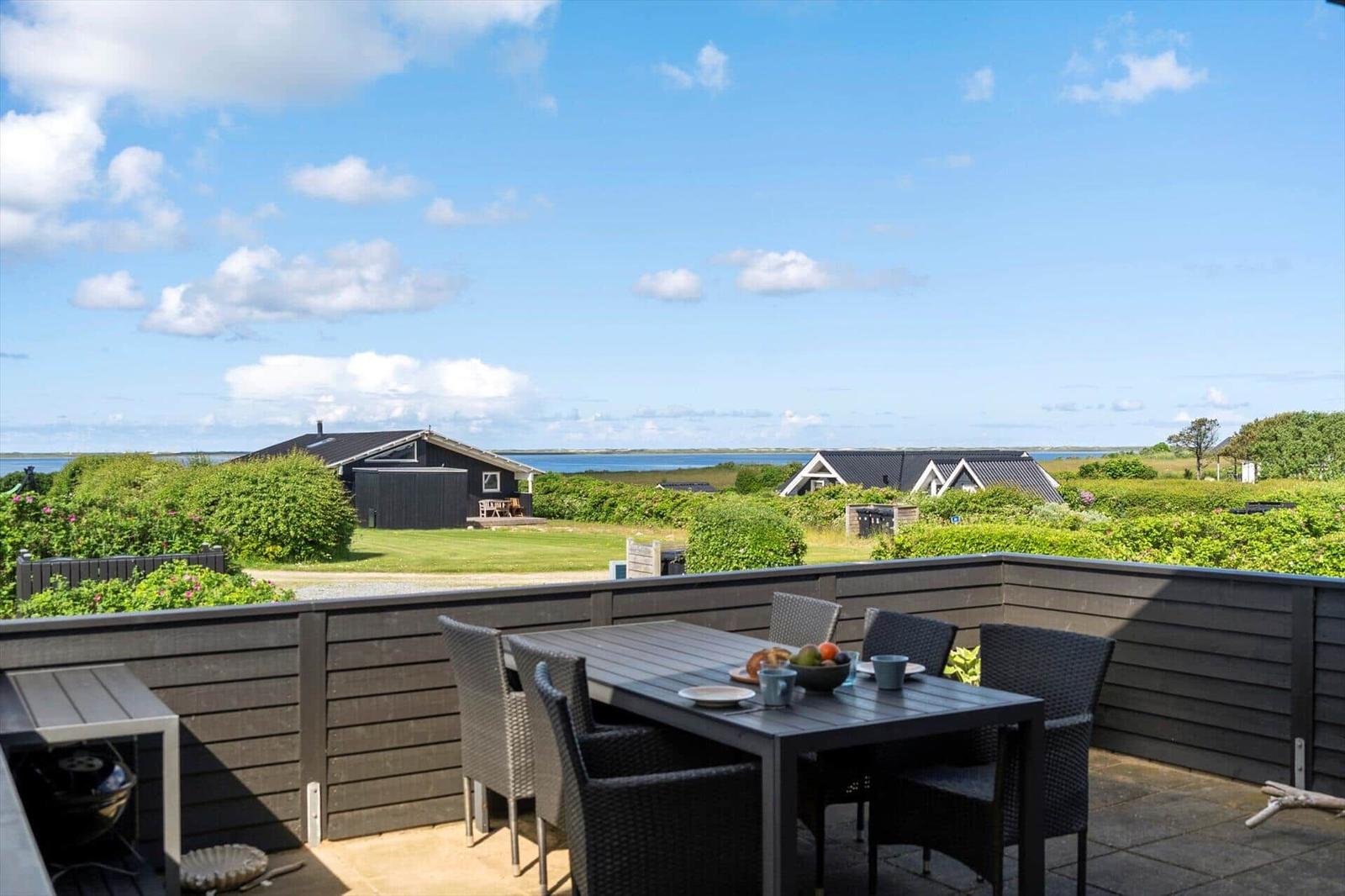 Terrace with table and chairs, view of green areas and water.