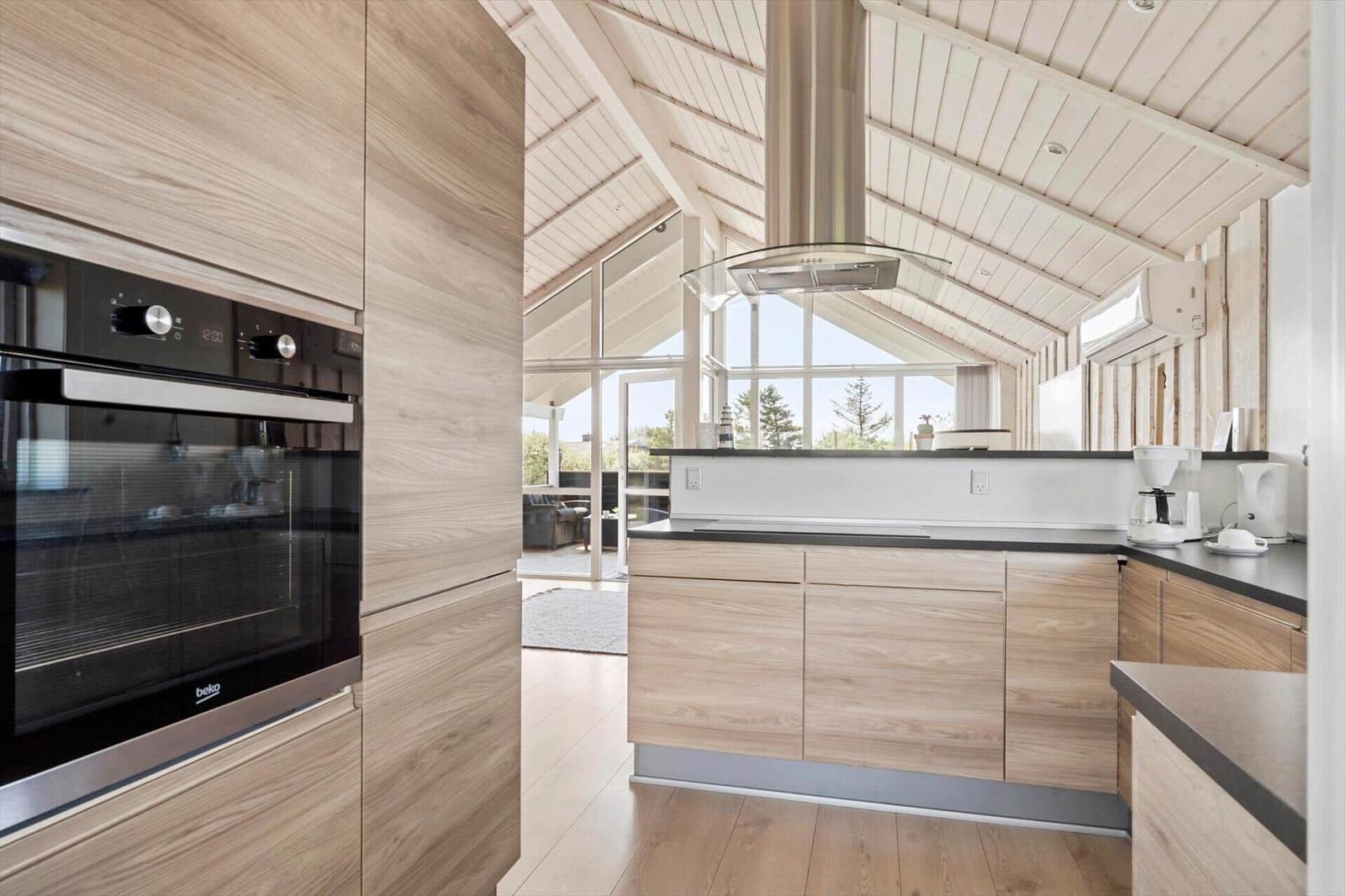 Moderne Küche mit Holzschränken und integriertem Backofen. Große Fenster bieten viel Licht.