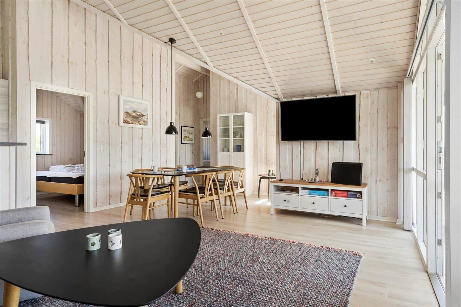 Wohn- und Essbereich mit TV, Esstisch und Schlafzimmer im Hintergrund.