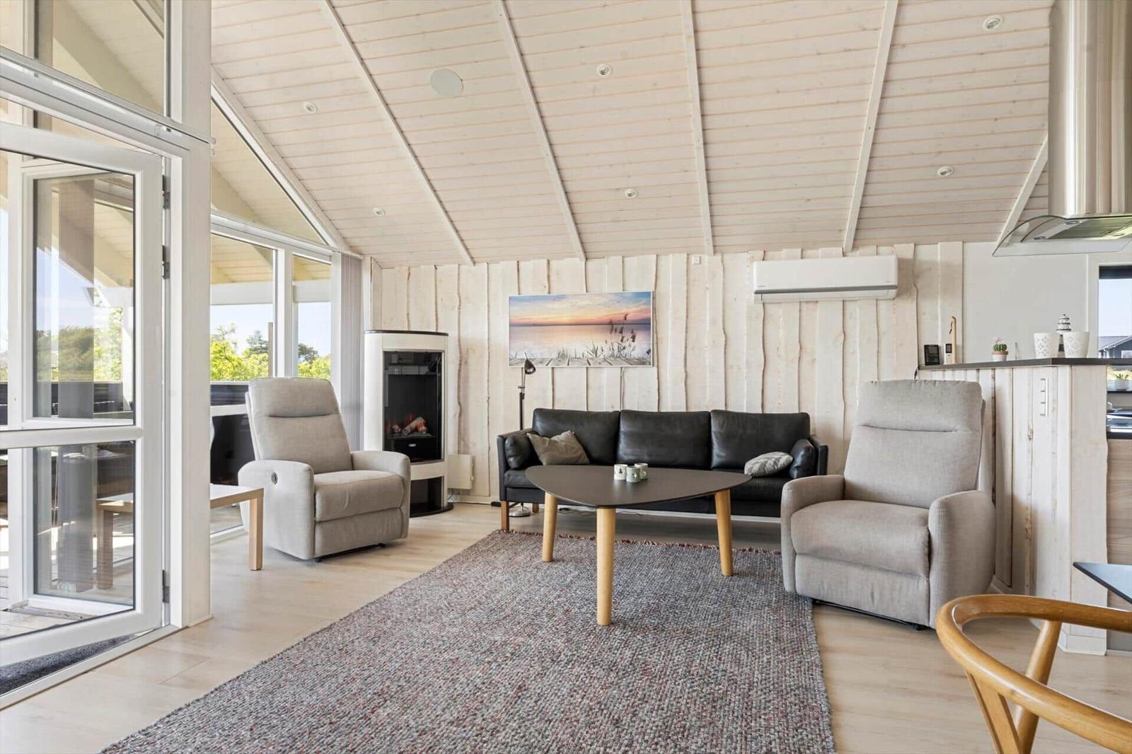 Wohnzimmer mit Sofa, zwei Sesseln, Kamin und Glasfront.