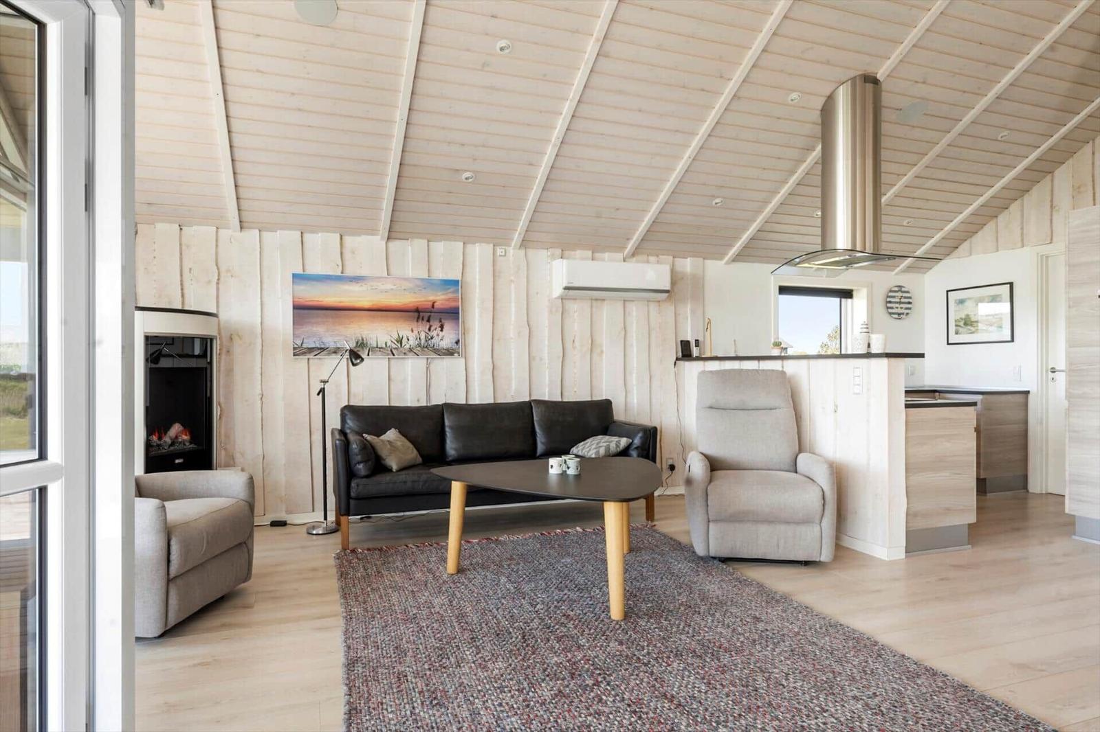 Wohnbereich mit Sofa, Sessel und Küchenzeile unter Holzdecke.