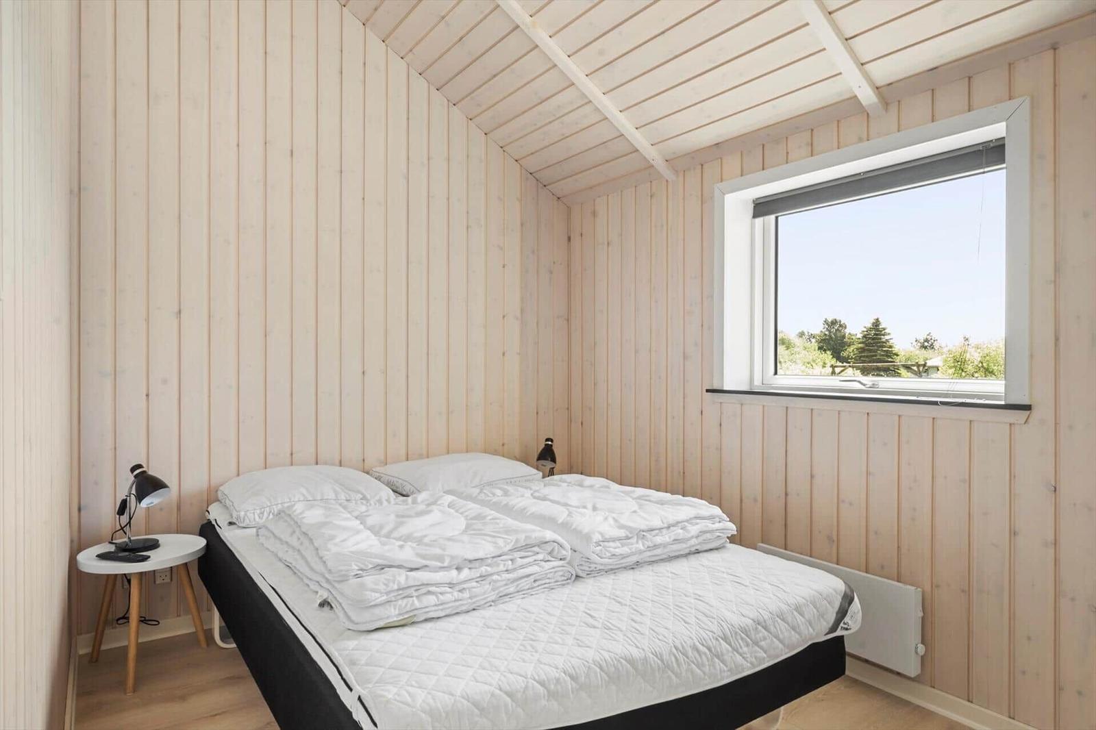Schlafzimmer mit Holzwänden, Bett und Fenster mit Blick auf Grün.
