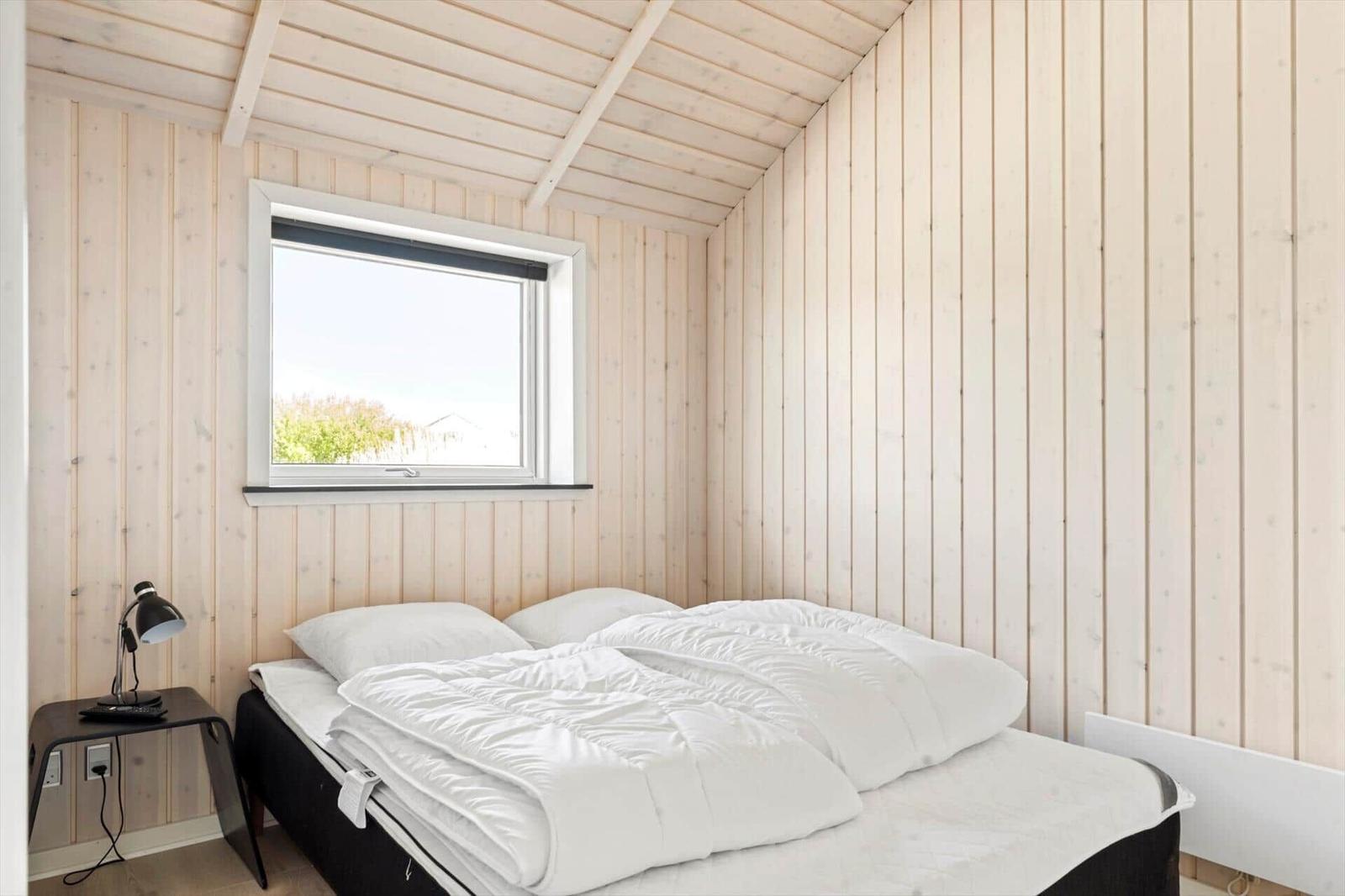 Schlafzimmer mit Bett, Fenster und Nachttisch.