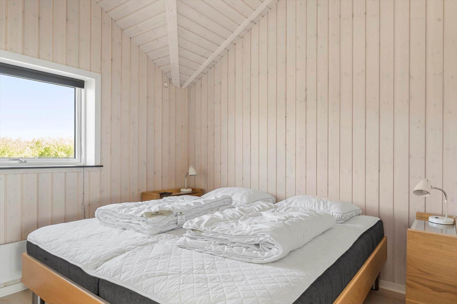 Schlafzimmer mit Holzwand, Bett, Nachttisch und Fenster.