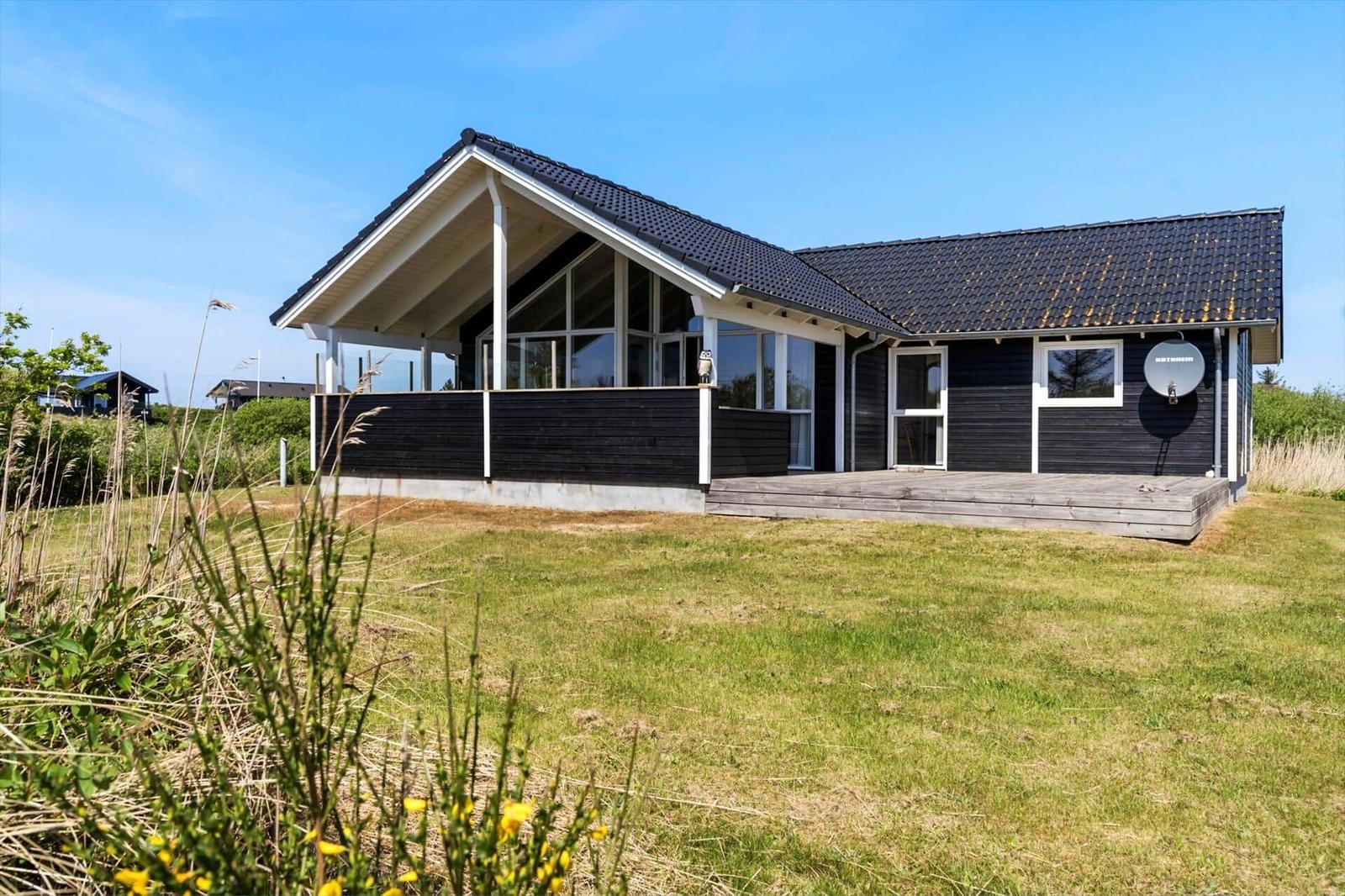 Moderne Villa mit Terrasse und Satellitenschüssel auf grünem Grundstück.