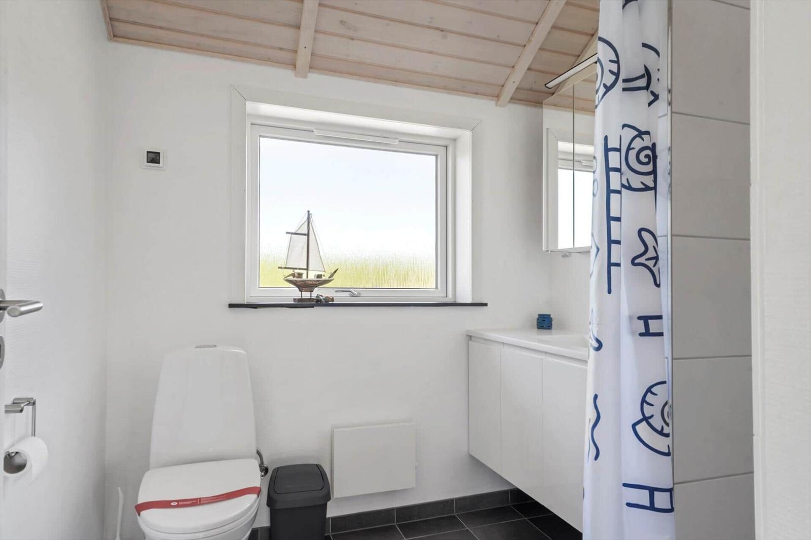 Badezimmer mit Toilette, Dusche und Fenster mit Segelyachtmodell.