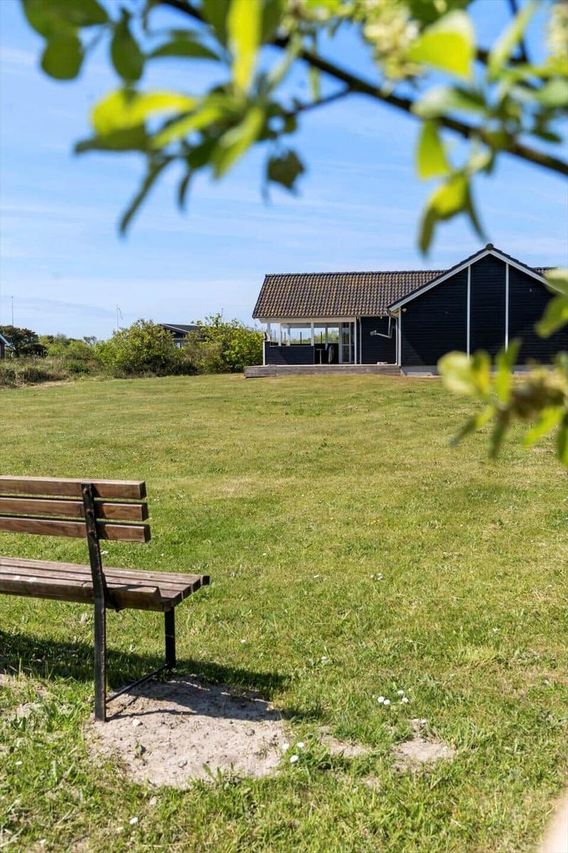 Holzbank vor grünem Rasen, schwarzes Haus mit Terrasse im Hintergrund.