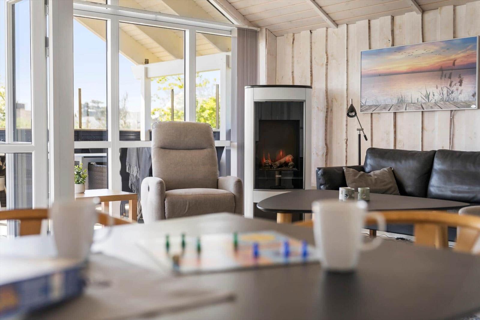 Wohnraum mit Kamin, Sofa und Sessel. Große Fenster und Wandbild sichtbar.