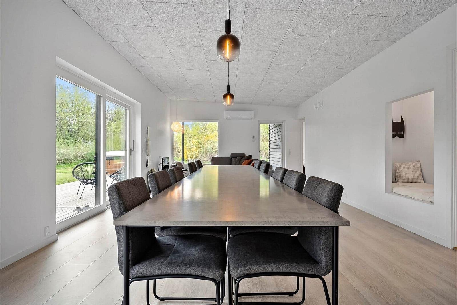 Langes Esszimmer mit Tisch und Stühlen, große Fenster und Schlafplatz im Hintergrund.