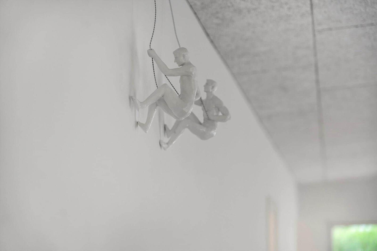 Zwei weiße Figuren hängen an Seilen an der Wand.