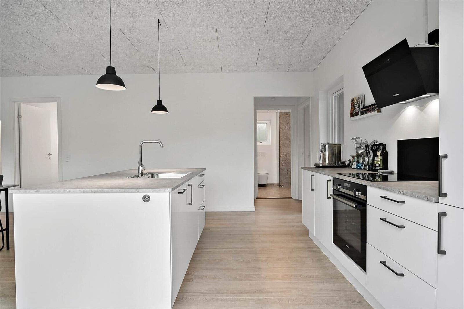 Moderne Küche mit weißem Schrank und Kücheninsel. Dunkle Hängelampen und Holzboden.
