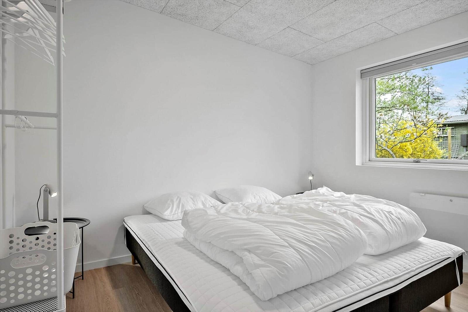 Schlafzimmer mit weißem Bett, Fenster und Kleiderschrank.
