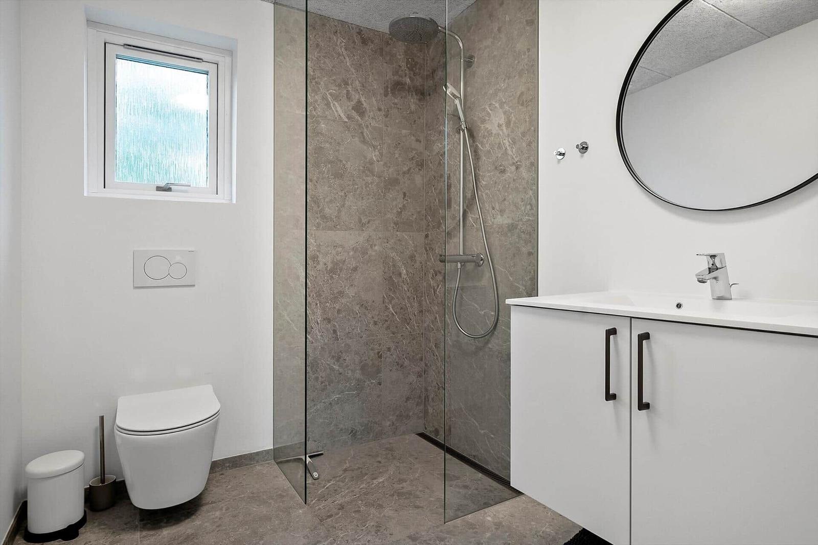 Badezimmer mit Dusche, Waschbecken und Toilette. Fliesen und Spiegel sind modern.