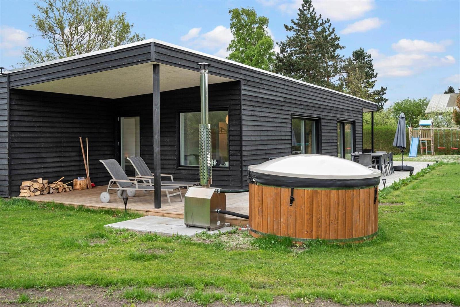 Moderne Holzhütte mit Whirlpool, Terrasse und Garten. Spielplatz im Hintergrund.