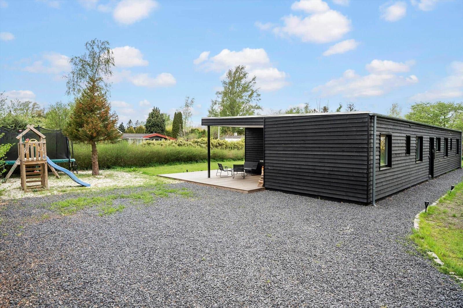Moderne schwarze Holzhütte mit Terrasse, Spielplatz und Grasfläche.
