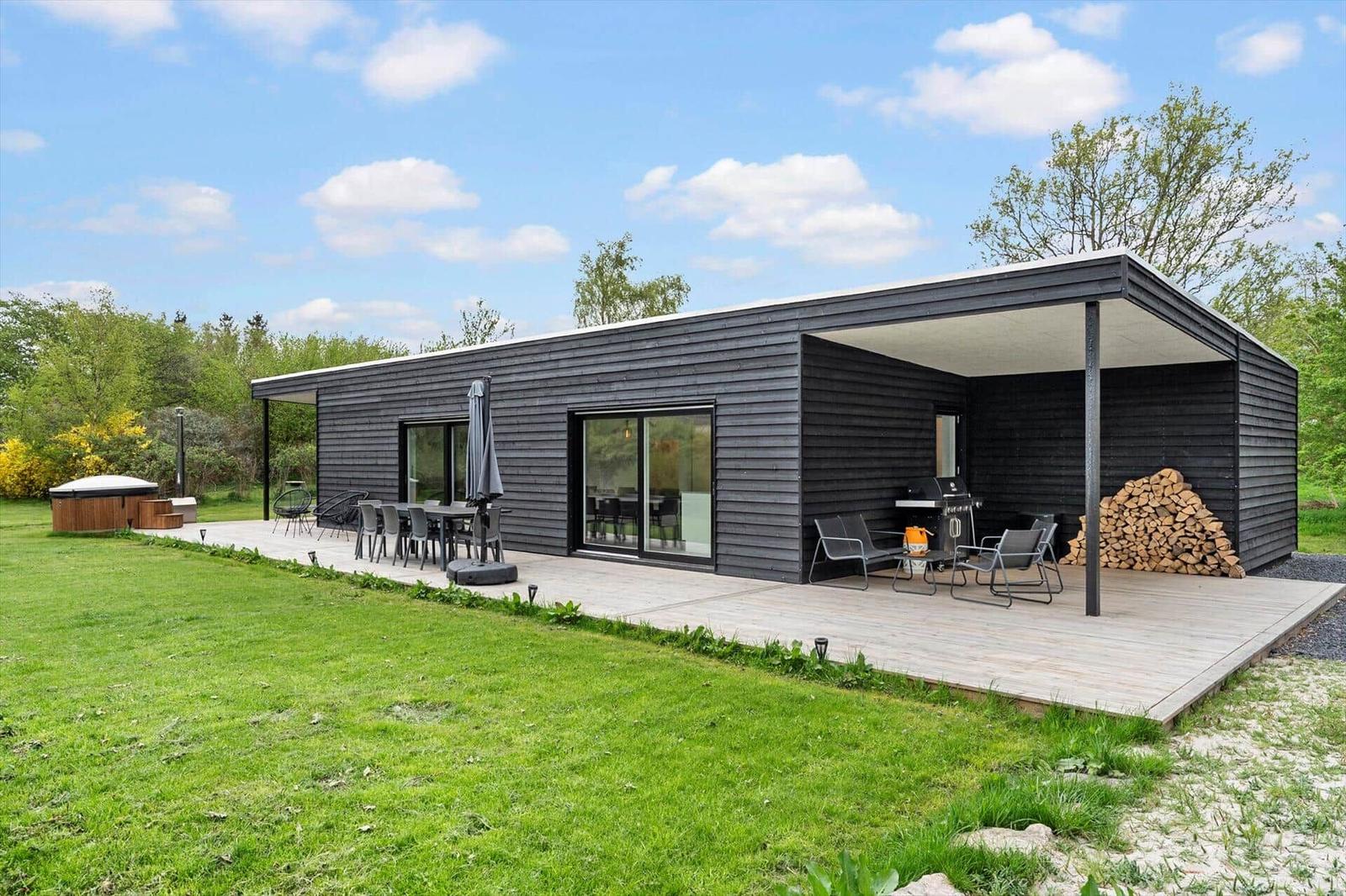 Moderne Villa mit Terrasse, Grill und Holzstapel. Grünflächen und Gartenmöbel.