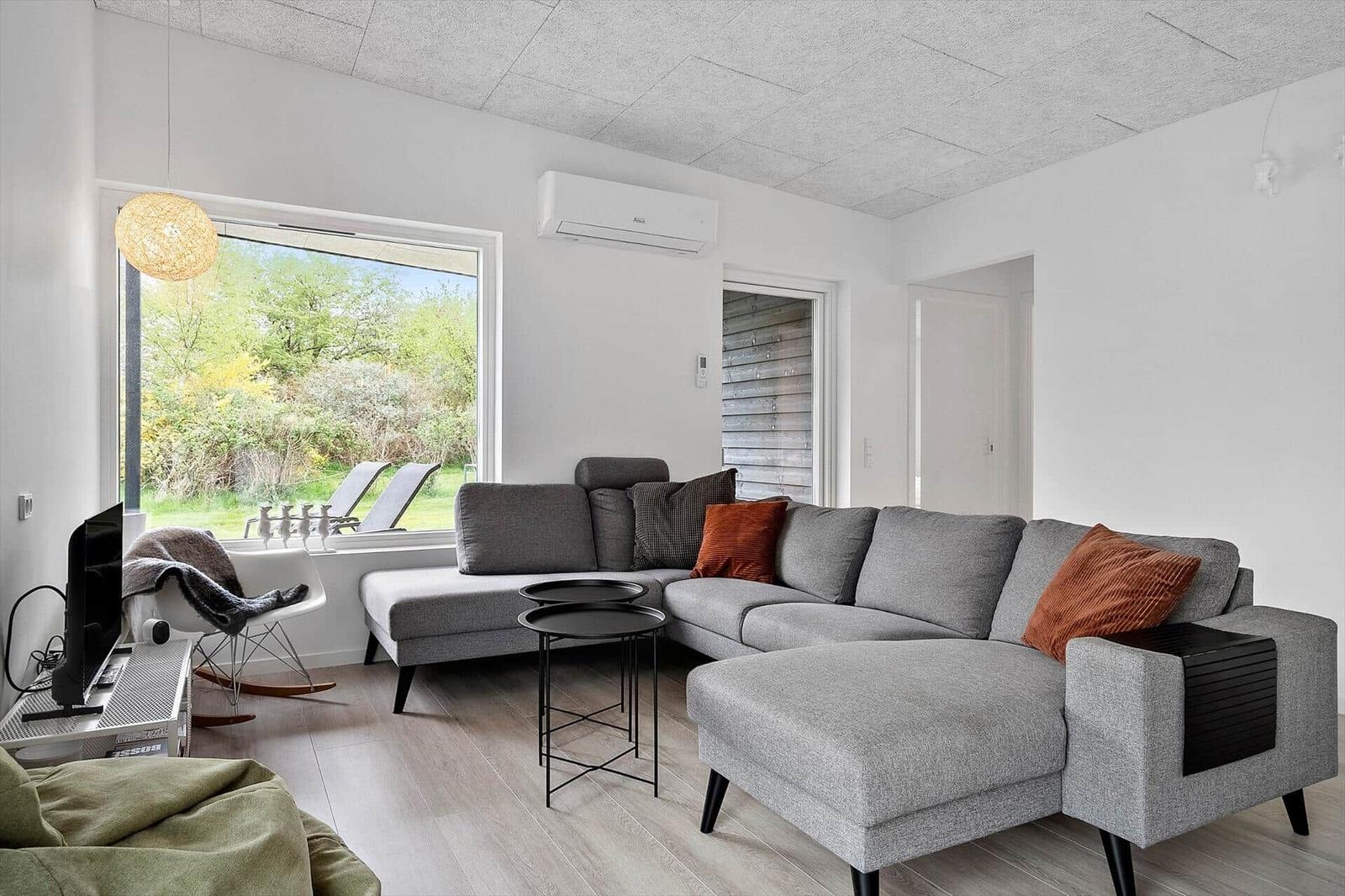 Wohnzimmer mit grauem Sofa, Fensterblick auf Garten und moderner Beleuchtung.