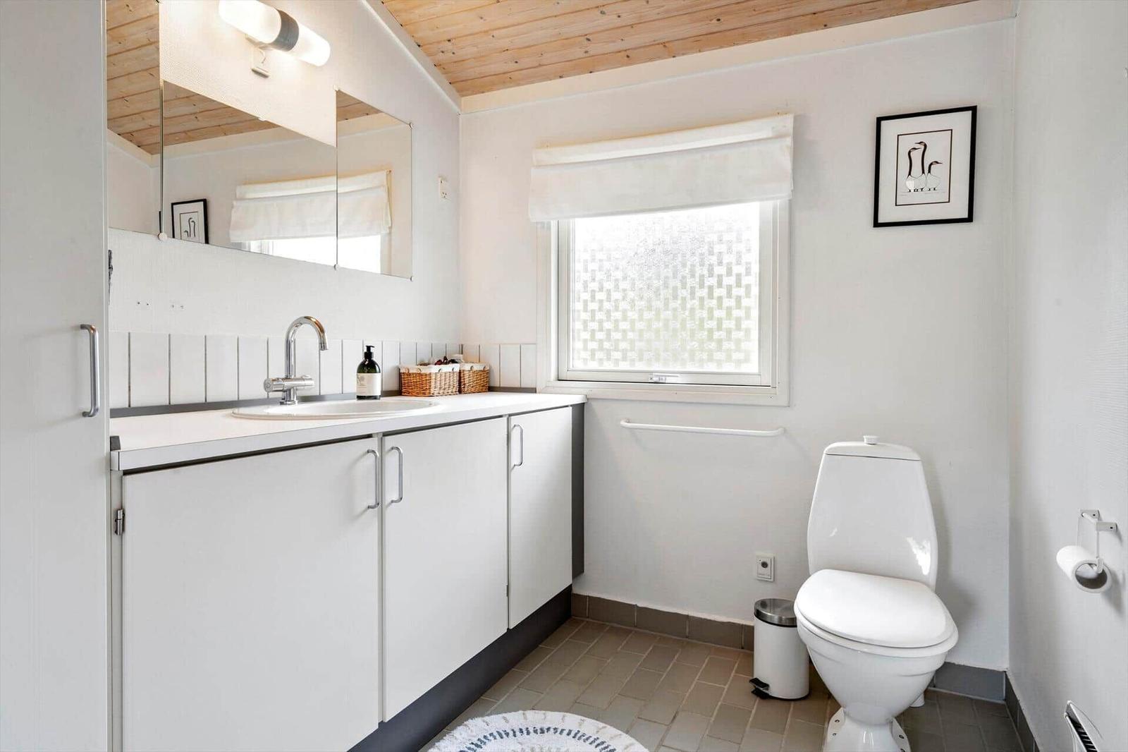 Badezimmer mit Waschbecken, Spiegel, Toilette und Fenster mit Rollladen.