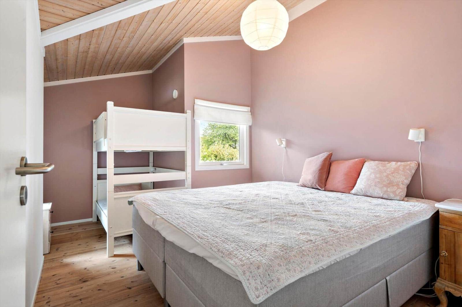 Schlafzimmer mit Doppelbett und weißen Kojenbett. Holzdecke und rosa Wände.