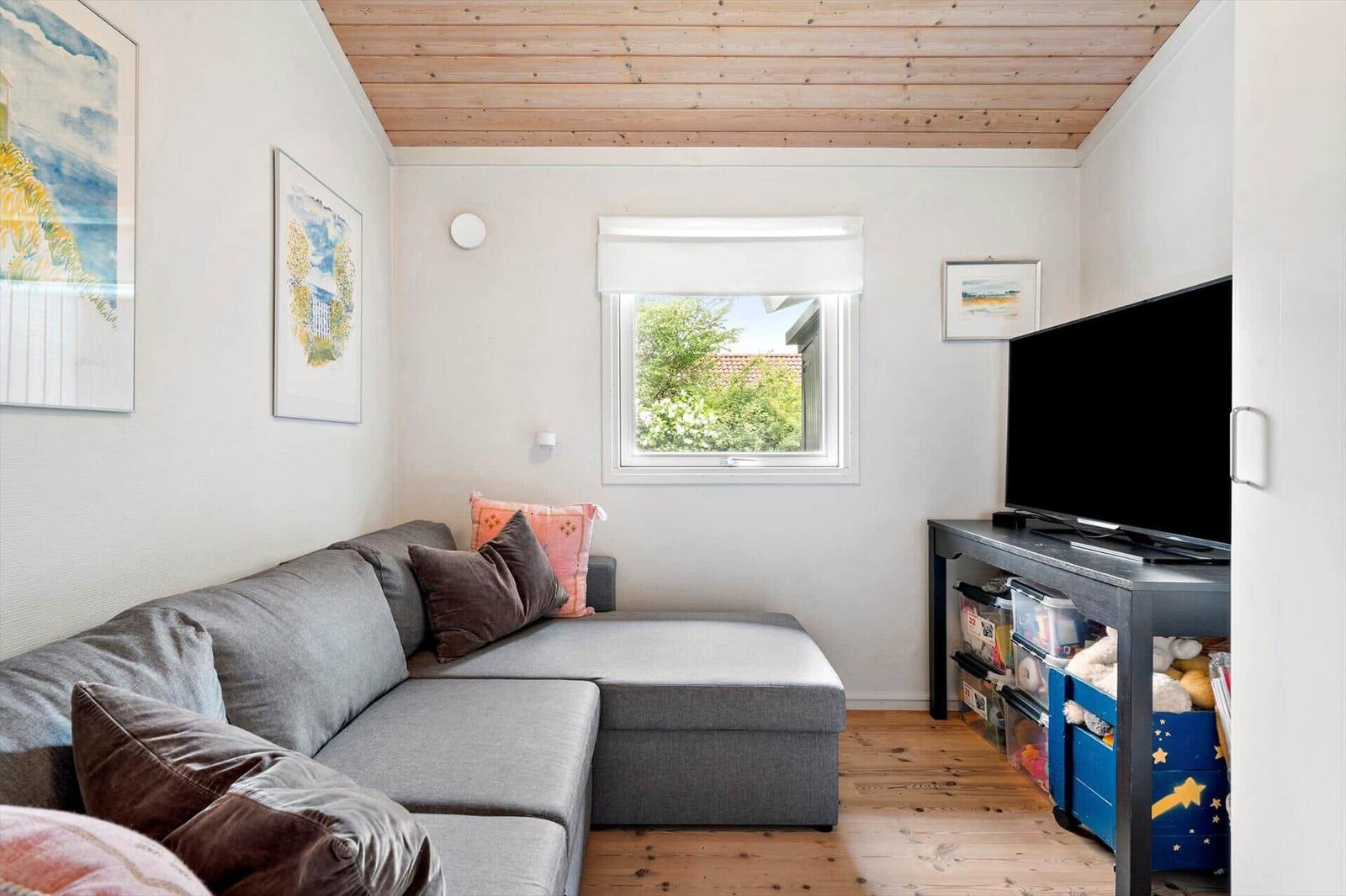 Ein Wohnzimmer mit grauem Sofa, Holzboden und Fenster. An der Wand hängen Bilder.