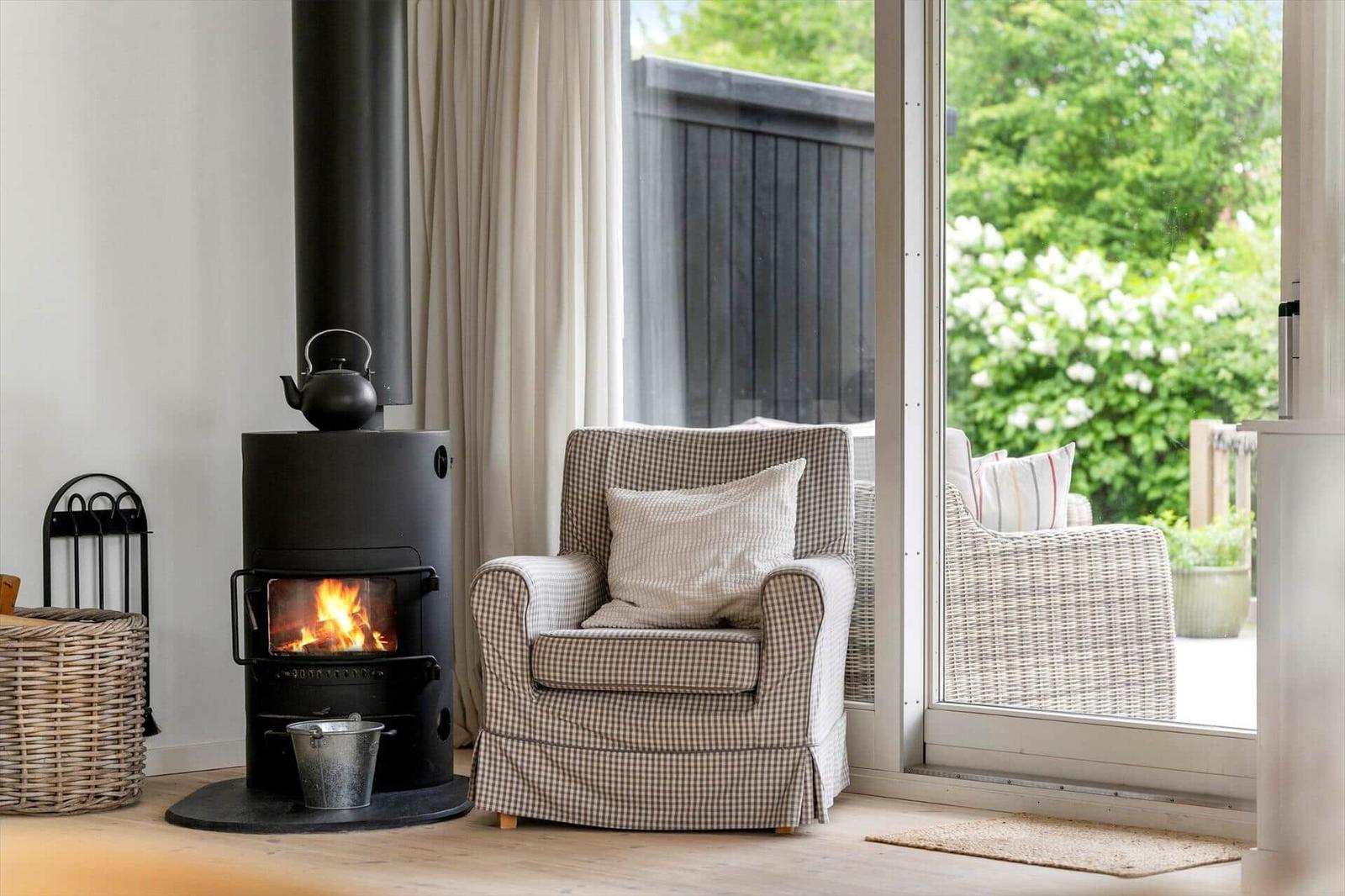 Ein Kamin mit brennendem Feuer, ein Sessel und eine Terrasse mit Blick auf Grün.