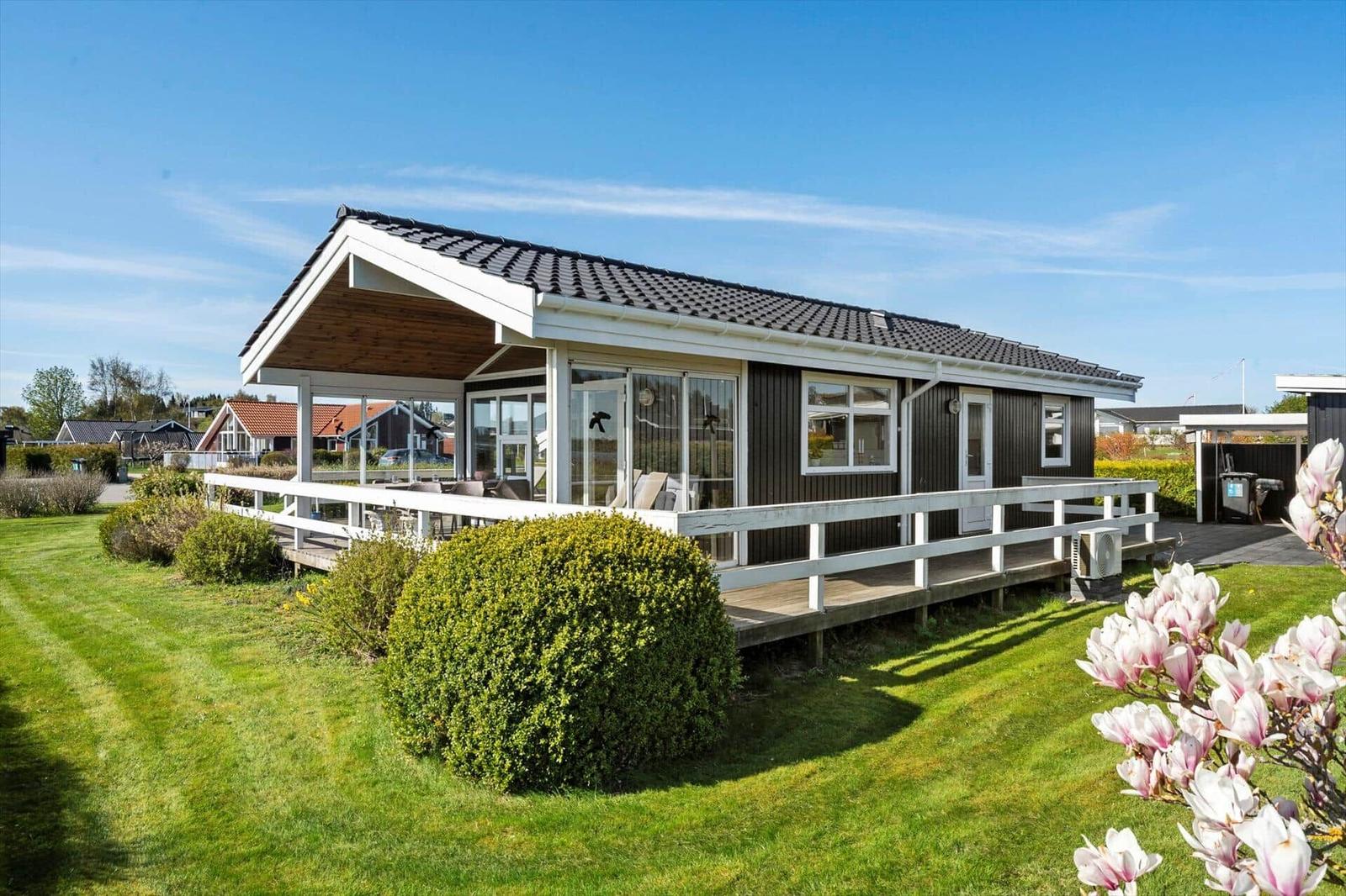 Modern holiday home with terrace and garden. View of the house with wooden veranda and green lawn.