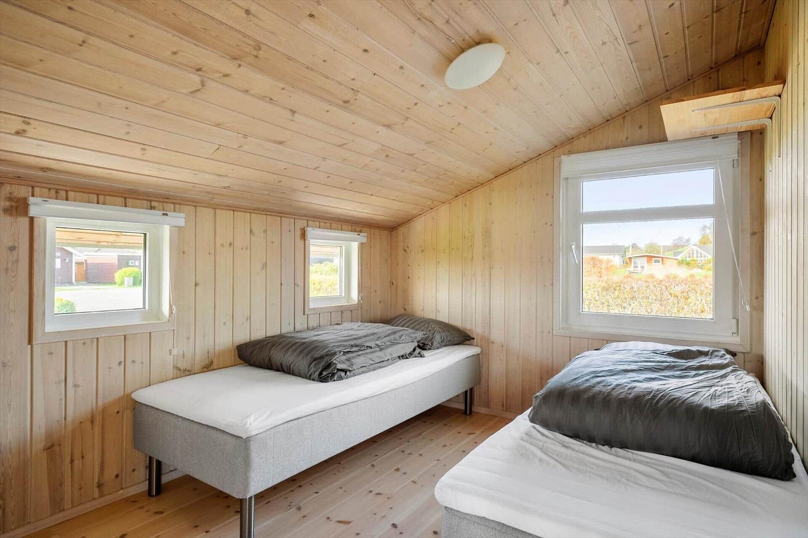 Two beds in a wooden house with windows and wooden ceiling.