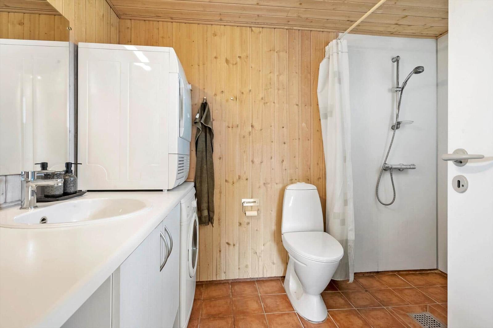 Bathroom with shower, toilet, and washing machine. Wooden wall and terracotta floor.