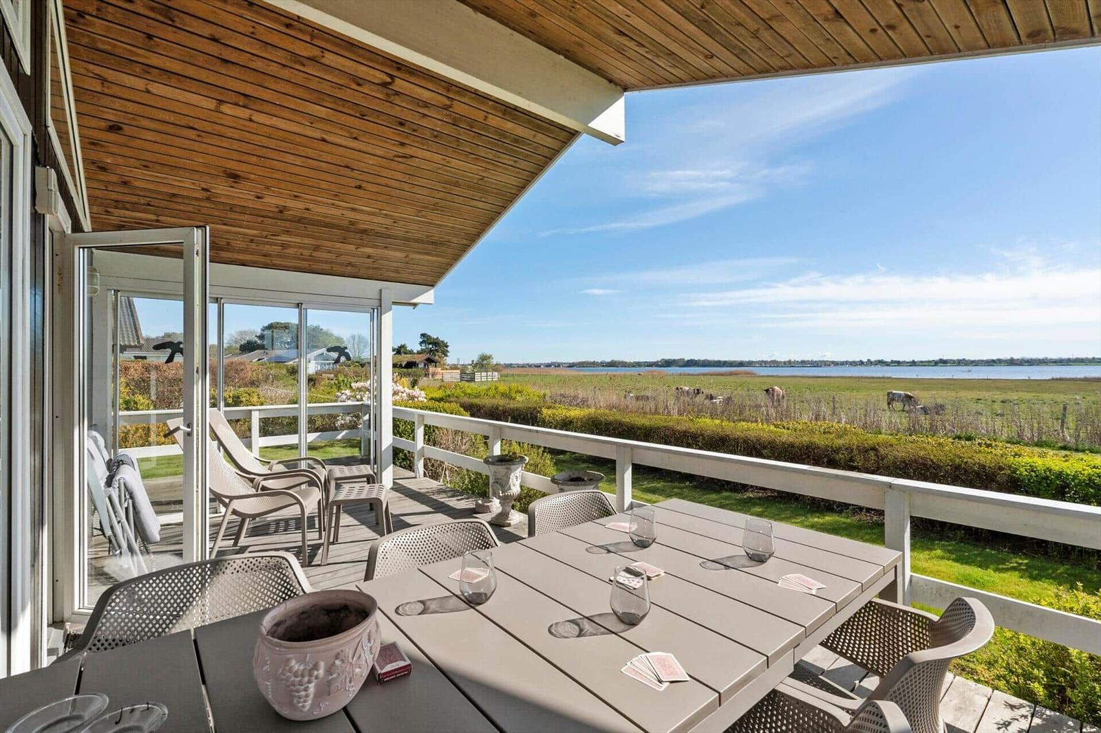Terrace with table and chairs, view of fields and water.