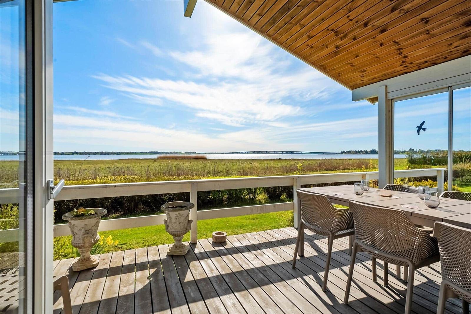Deck with table and chairs, view of water and grassland.