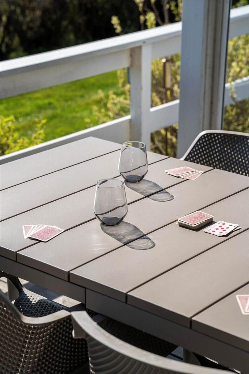 Outdoor table with glasses and playing cards on terrace with view of green area.