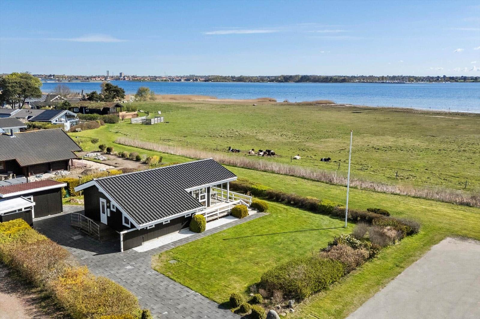 Modern house with terrace, surrounded by green areas and a lake.