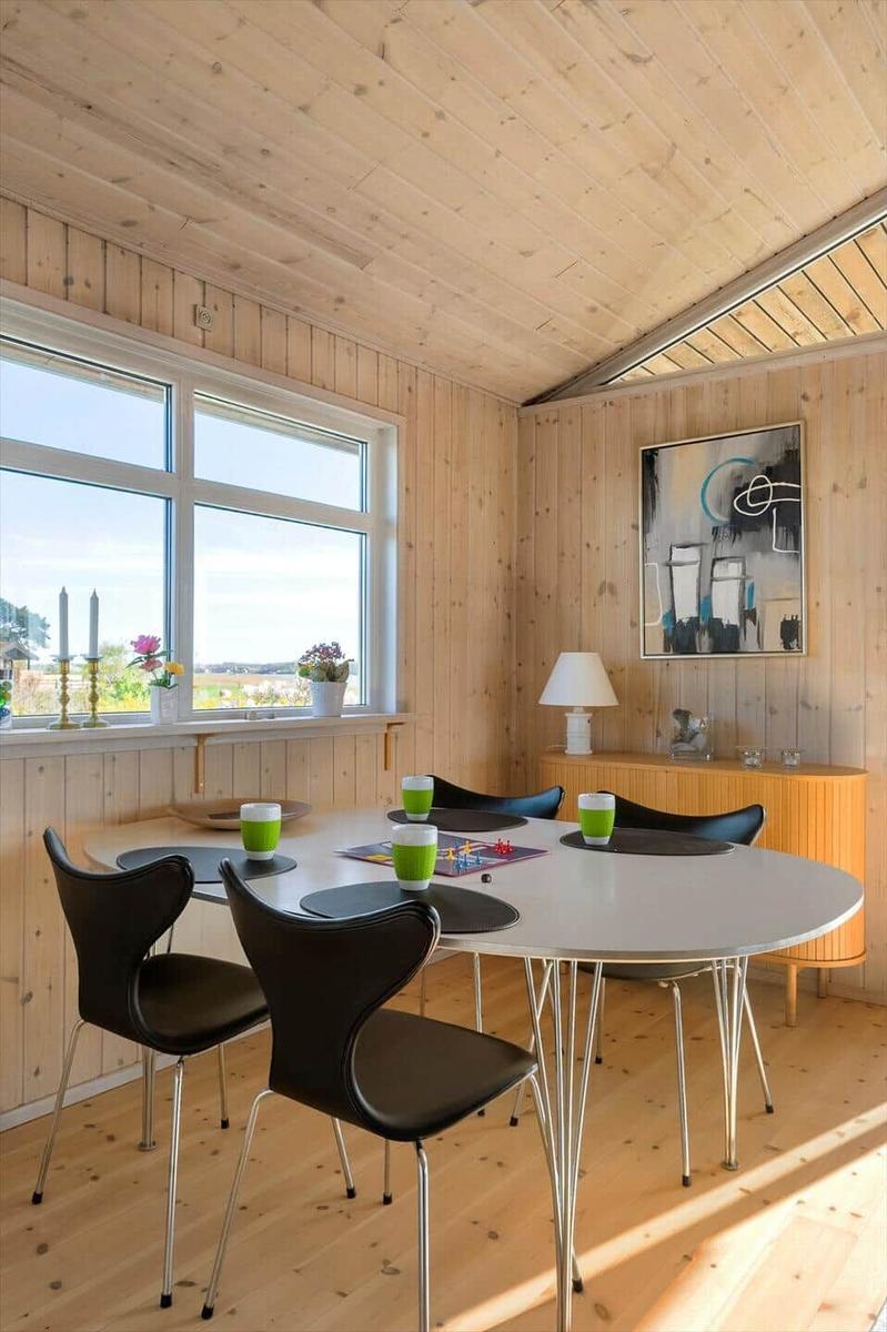 Round dining table with black chairs and green cups. Wooden walls and large window with view.