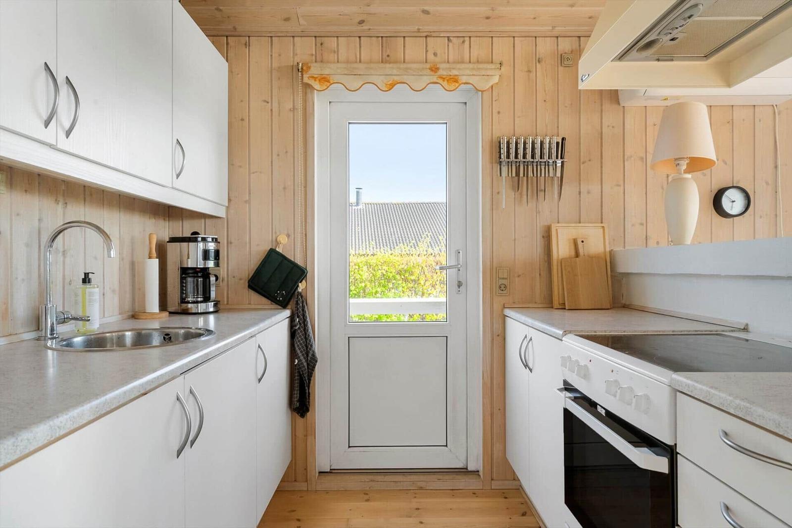 Kitchen with white cabinets, stainless steel sink, and door to balcony.