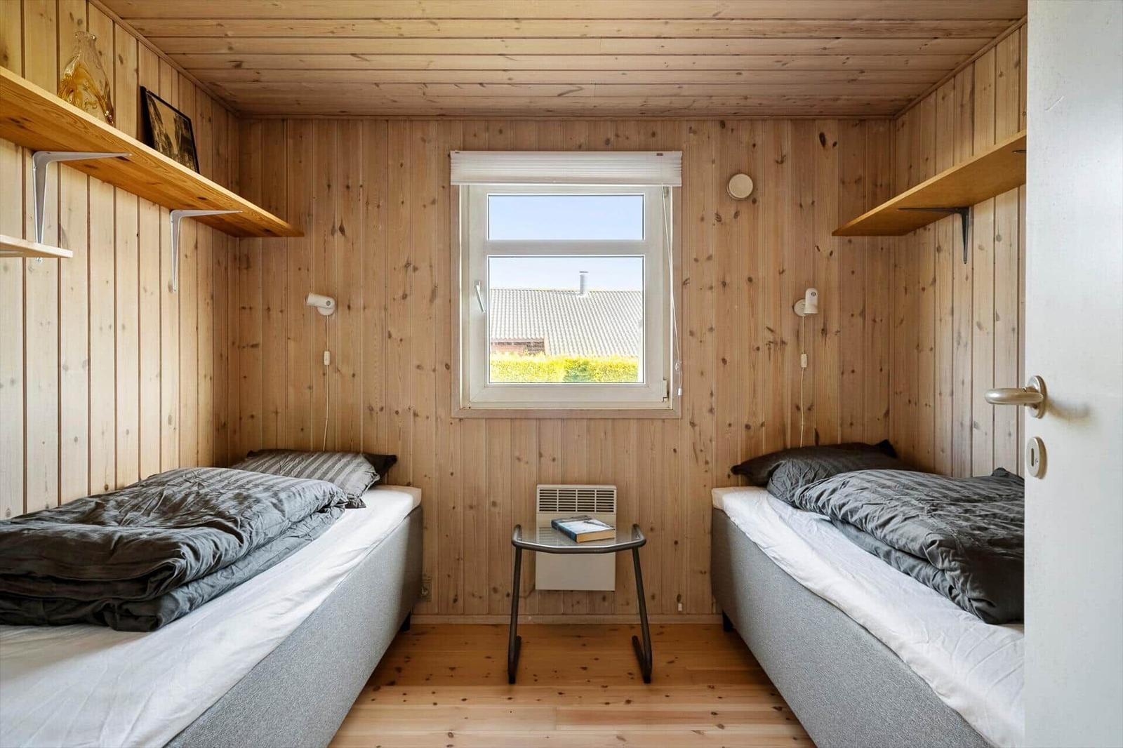 Two single beds in a wooden room with window and small table.
