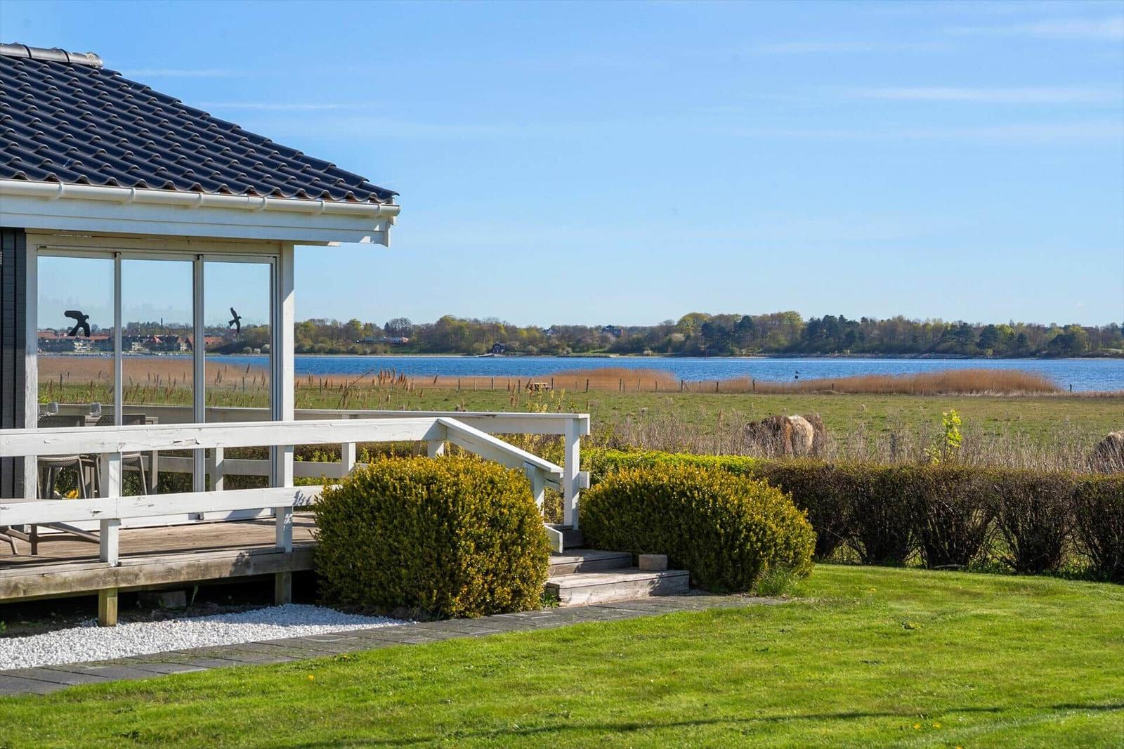 House with terrace and view of a lake with shoreline vegetation.